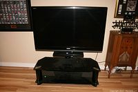 Front view of Toshiba Regza 52 inch HDTV on Tech Craft glass stand in a room with hardwood floor and vintage furniture.