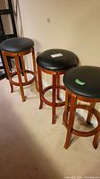 Three wood barstools positioned side by side against a wall