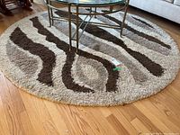 Wide angle view of the round carpet under a coffee table showing the neutral tone brown and cream wavy stripe pattern on a hardwood floor.