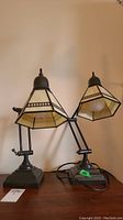 Pair of adjustable desk lamps made of metal with stained glass style resin shades on wooden surface.