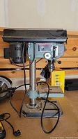 Side view of Delta drill press showing motor housing, column and base along with attached power cord.