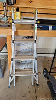 Front view of folded aluminum ladder showing rungs and frame inside a garage workshop environment.