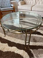 Round glass coffee table with metal frame and claw-foot legs on a patterned carpet.