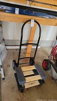 Small black metal hand truck with curved handle and two wheels at base