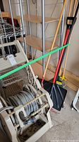 Wide view showing hose reel on wheels with hose, snow shovel, and two rakes standing beside it.