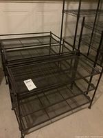Three matching black metal shoe racks with 3 mesh shelves each, placed together in a room with white paneled door background.