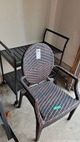 Resin wicker patio chair with oval backrest and armrests in front, black metal bar cart behind