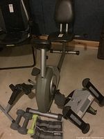 Side view of Stamina Magnetic Recombinant exercise bike with seat, backrest, and pedals, along with two hand weights and one leg weight set.