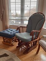 Wooden rocking chair with blue upholstered cushions and matching ottoman in front of window.