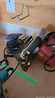 Photo showing Mastercraft electric palm sander with blue base and dust vent next to Chicago Electric circular saw
