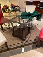 Round table with beveled glass top and wooden base surrounded by chairs and clutter, showing overall condition and setup.