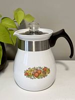 Front view of the white ceramic tea pot with floral design, black handle, glass lid, and stainless steel band.