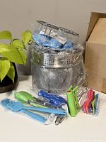 Photo showing the full Instant-Pot accessory set including baskets, utensils, whisk, measuring spoons, and silicone holders arranged on a table.