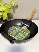 Clear top-front view of the black stir fry pan showing label and handle.