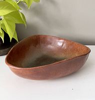 Triangular shaped pottery bowl showing glazed surface in brown and green earth tones with smooth finish