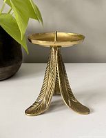 Front view of brass candle stick holder with decorative curved legs and a spike in the center for securing a candle.