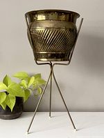 Front view of the vintage brass plant pot raised on a tripod stand, showing textured diagonal ridges and aged brass patina.