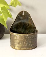 Front view of vintage brass wall pocket hanging plant holder with visible patina, measuring approximately 6.5" tall and oval-shaped container.