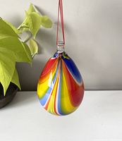 Front view of the pear-shaped glass hanging ornament displaying vibrant red, yellow, blue, and white swirled colors with a red ribbon attached at the top.