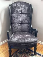 Front view of the vintage armchair showing black crushed velvet tufted cushions with solid wood frame and floor rug beneath.
