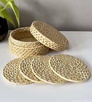 All 4 flat round woven wicker coasters laid out in front of the matching lid and container.