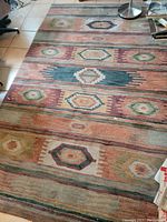 Rectangular rug with repeating geometric hexagonal patterns in earth tones, laid on tiled floor, showing signs of wear and discoloration