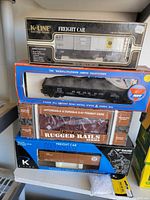 Stacked boxes containing four O-27 gauge model train freight cars, visible through display windows showing the train cars' details