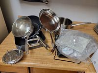 Overview of multiple stainless steel cookware items including pots, pans, lids, and steamer insert on a wooden surface.