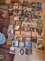 Overview of approx 45 music CDs arranged on a floor, showing jewel cases and cover art. Mix of rock, pop, and classical genres visible.