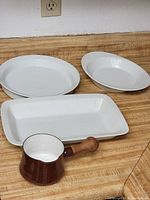 Four white ceramic plates: two round, one oval, one rectangular, on wood surface with an electrical outlet in background
