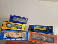 Photo of five boxed model freight cars arranged together showing brand logos and model details.