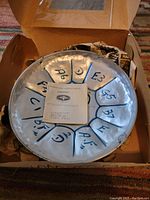 Steelpan drum top view showing musical note markings and instruction sheet in box.