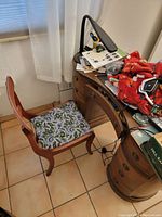 Photo showing overall view of vintage wooden desk with clutter on top and accompanying wooden chair with blue floral cushioned seat.