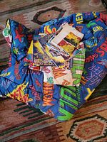 Photo of colorful vintage Marvel blanket with bold character names and comic text, with folded Marvel comic fabric pieces on top.