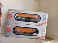 Two boxed Williams Classic Freight Series model train freight cars, one orange, one yellow-orange, in original packaging.
