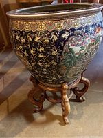 Full view of porcelain fish bowl seated on carved wooden stand