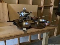 Full set of six copper pans and pots with chafing dish on wooden surface showing overall lot.
