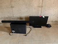 Samsung 27 inch TV, sound bar, and subwoofer arranged on floor, showing power cables and setup.