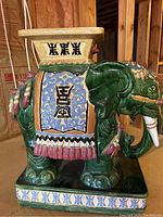 Side view of green glazed pottery elephant table showing detailed saddle cloth with Asian characters and ornamental features.