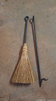 Photo of fireplace broom and poker resting on concrete floor showing handles and tool heads