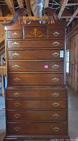 Front view of the tall two-piece highboy chest of drawers, showing brass drawer pulls, floral inlay on center drawer, scratches, and overall condition.