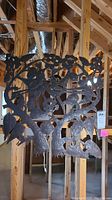 Full view of the square metal wall art with bird and floral cutout design hanging among wooden beams