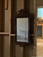 Full view of rectangular beveled mirror in ornate, carved wood frame mounted on unfinished wall.