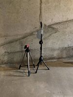 Wide view of two tripods against a concrete wall, showing height difference and leg design.