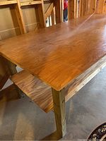 Close-up photo showing the large wooden work table surface, legs, and lower shelf in a basement setting.