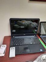 Front view of Dell laptop with keyboard and screen, showing 16-inch display size and dust on the screen, with no power cords visible.