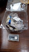 Clear plastic container holding multiple white electric duplex outlets and a small box with miscellaneous electrical components.