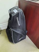 Black Reebok hockey equipment bag standing upright, showing side mesh compartments and top handle.