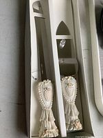 Two resin wedding cake cutters with decorative handles featuring hearts and floral accents, in white storage box.