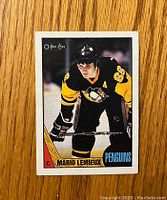 Front view of 1987-88 O-Pee-Chee Mario Lemieux hockey card showing player in Penguins uniform with logos and card number.